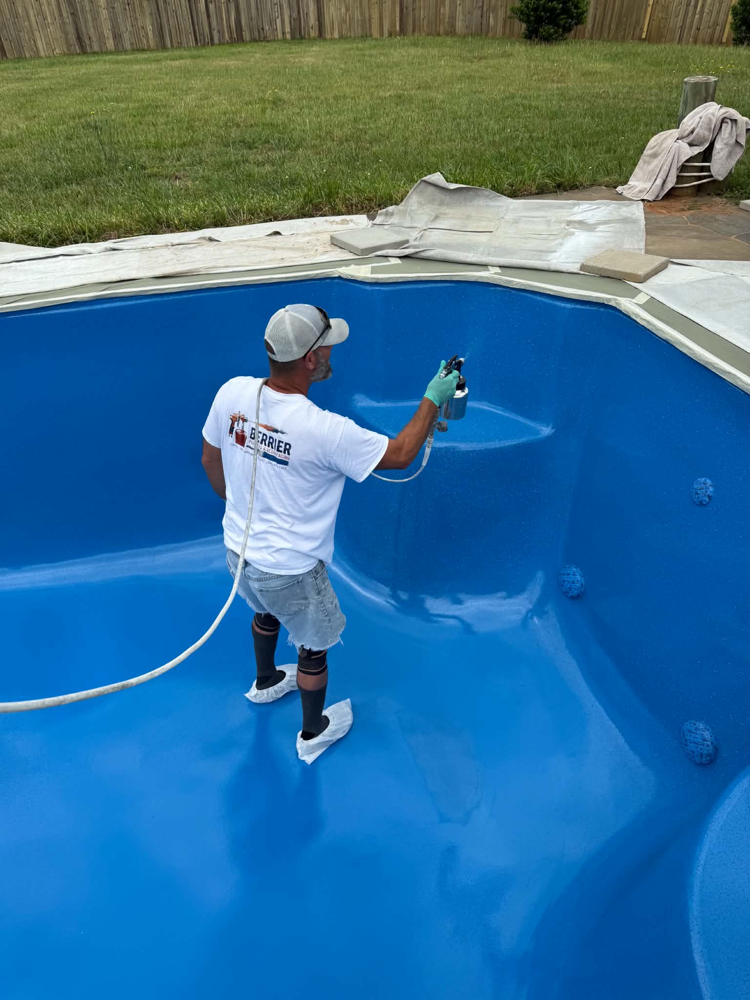 Technician spraying a blue fiberglass pool