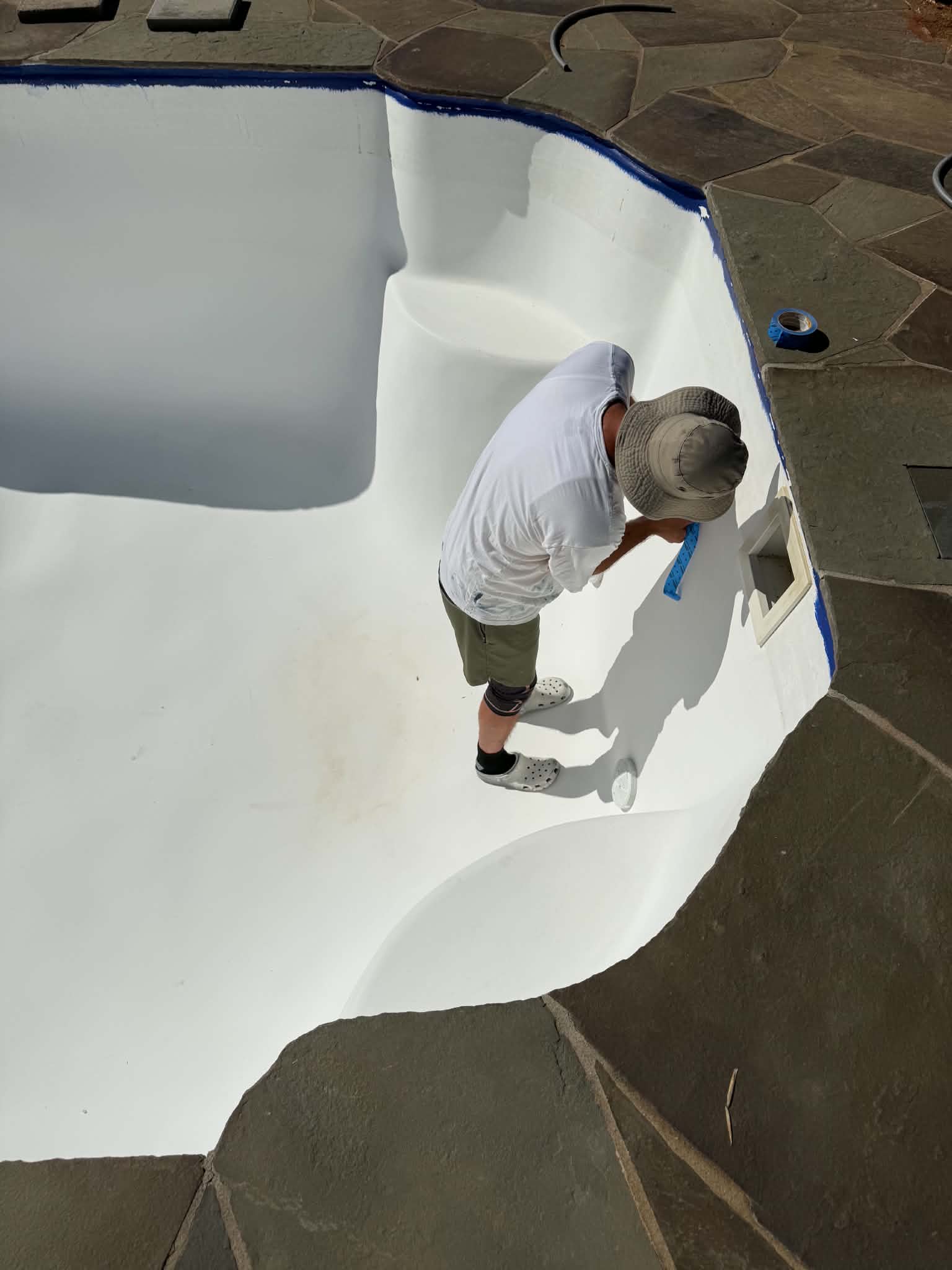 Technician applying a white coating inside a pool